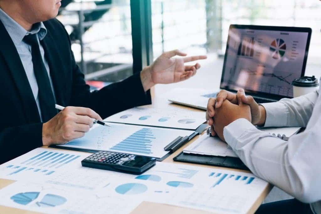 Two business professionals analyzing social media analytics and key performance indicators (KPIs) during a meeting, discussing engagement metrics, ROI, and audience targeting strategies.