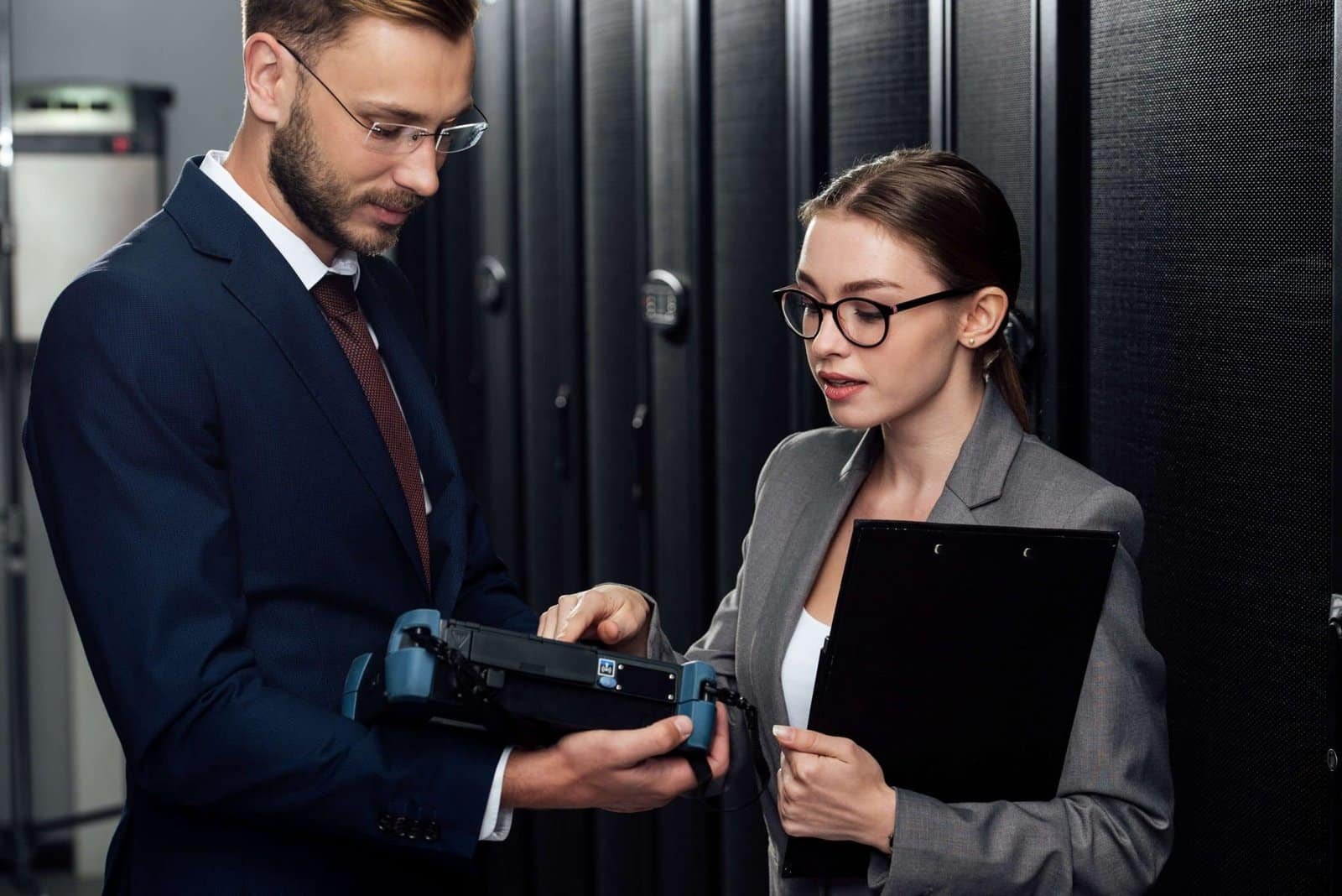 A professional man and woman in business attire focus on a computer screen, engaged in a work-related discussion.