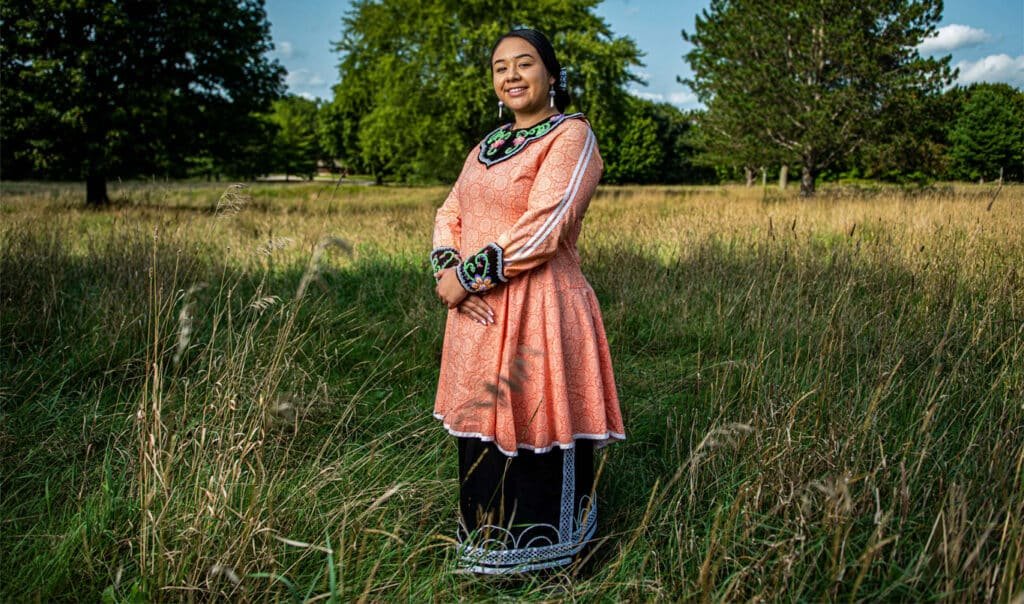 A young Oneida Nation citizen in traditional regalia, standing in a field on Oneida Nation land