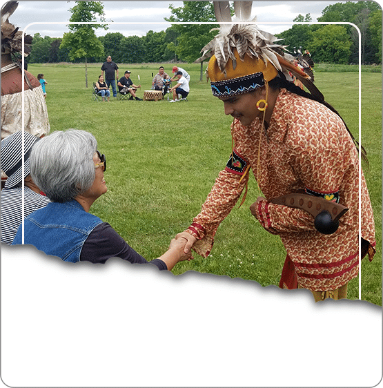 An Oneida Nation community member in regalia greeting a visitor at a community event