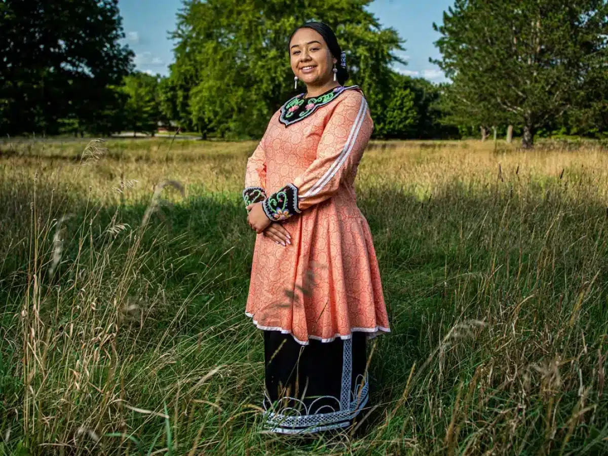 Oneida Nation community member in traditional regalia standing in a meadow
